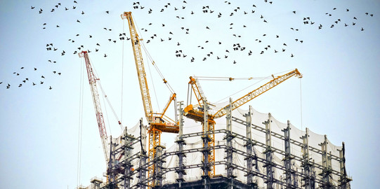 Es ist eine Baustelle mit Kränen zu sehen, sinnblidlich für ein lange andauerndes Projekt