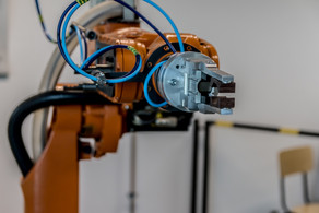 Roboterarm Zu sehen ist ein orangener Roboterarm mit einer Greifzange die an mehrere Schläuche gebunden ist.