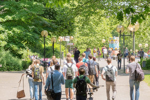 Studierende am Campus Nord Studierende laufen über den Campus Nord. Es ist eine große rote Skulptur in Form von großen Zahnrädern zu erkennen.